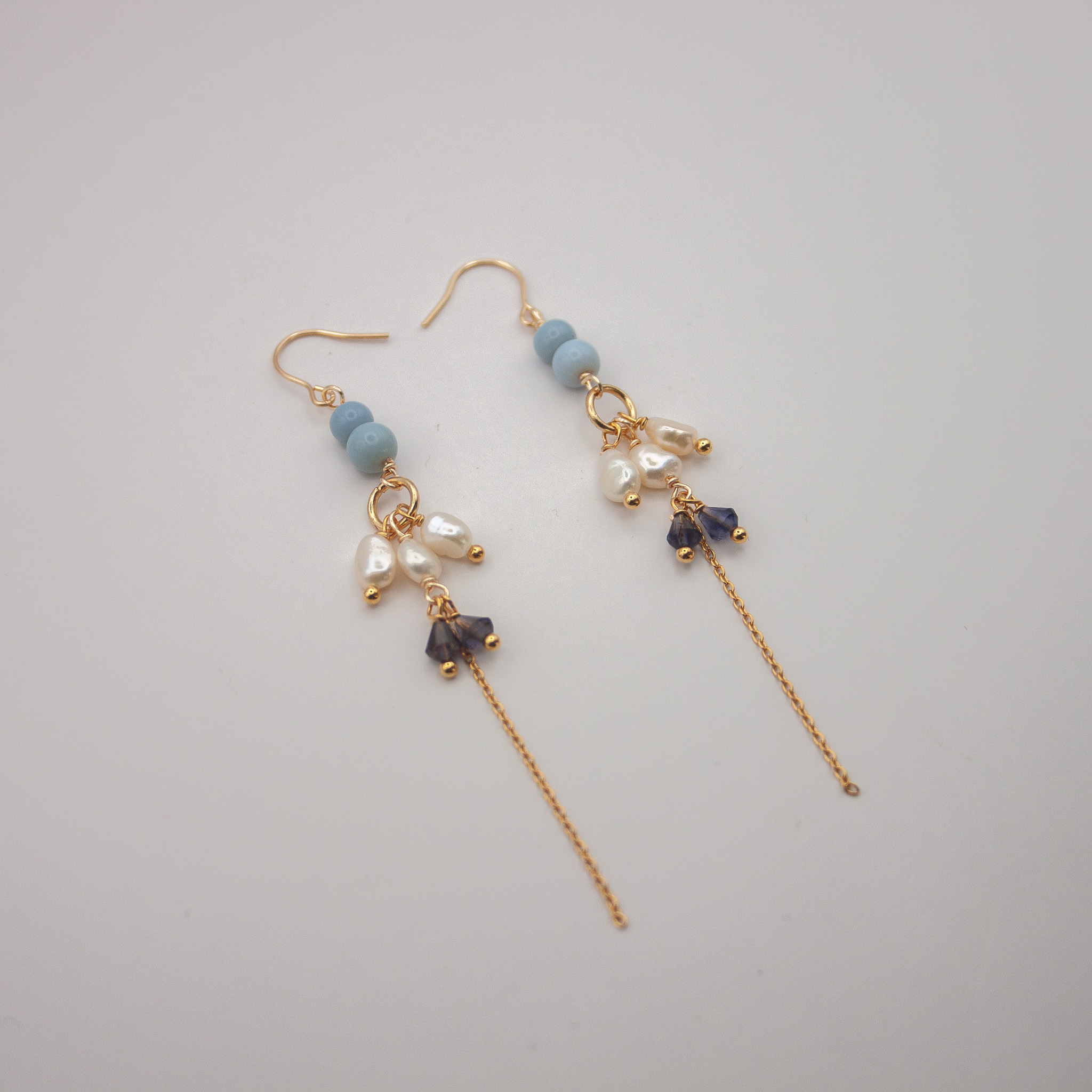 Gouden oorbellen met lichtblauwe kralen, witte parels, donkerblauwe kristallen en een lange fijne ketting
